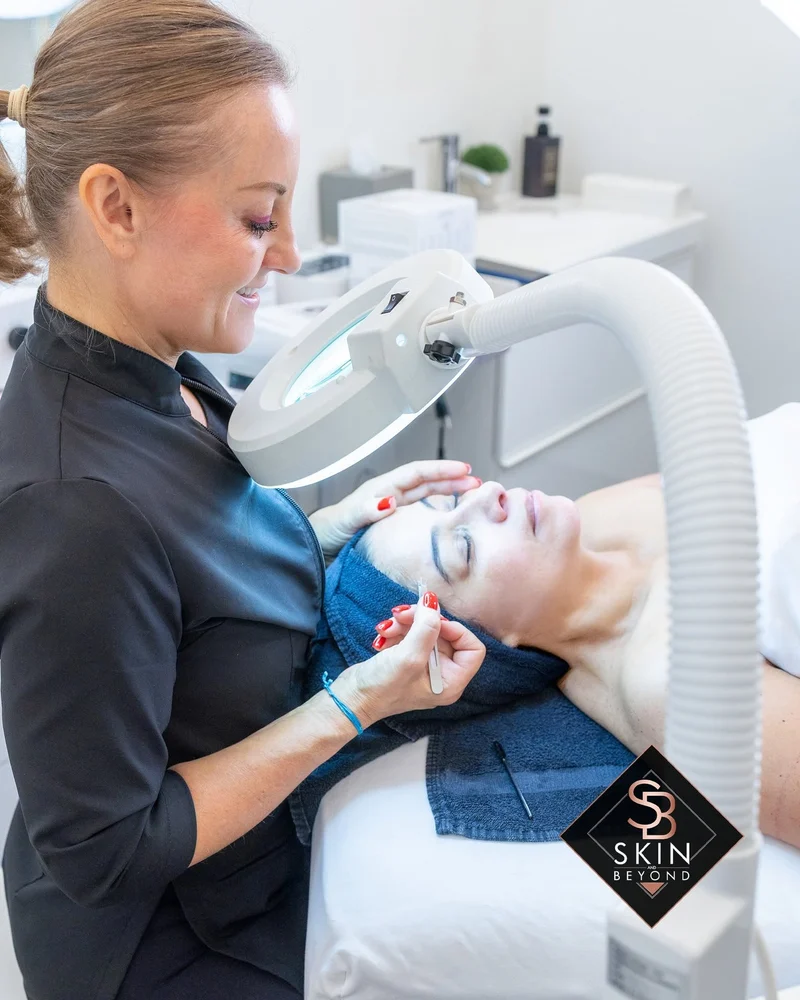 Brow shaping with magnifying lamp during a facial at Skin and Beyond Spa